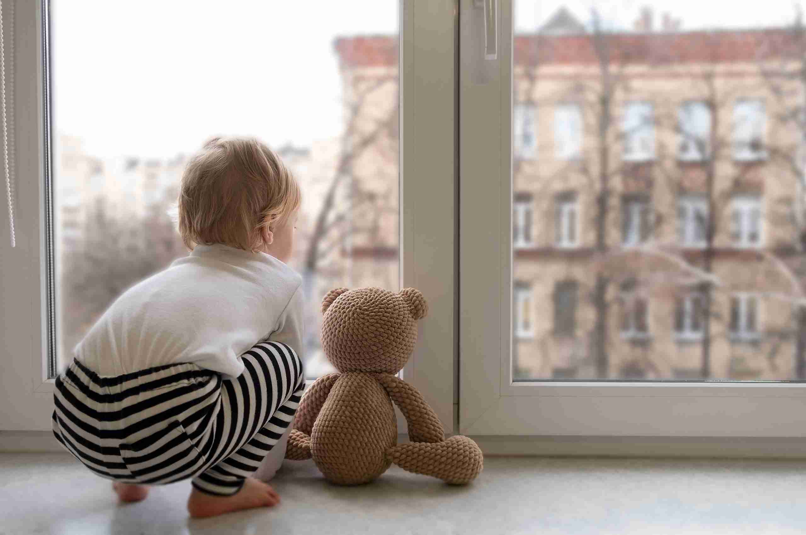 baby with toy sitting on window ledge